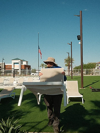 Technician carrying a white lounge chair back into position on cleaned artificial turf