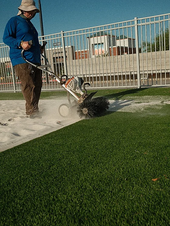 Technician running a power broom along the border where volleyball sand meets artificial turf at Revel Surf