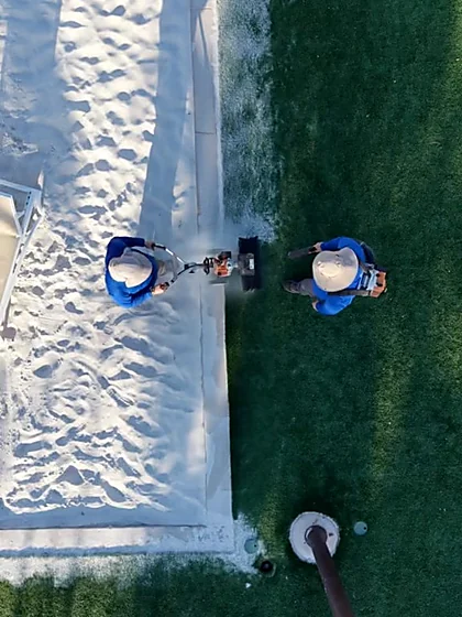 Overhead view of two technicians working the border between sand court and synthetic turf