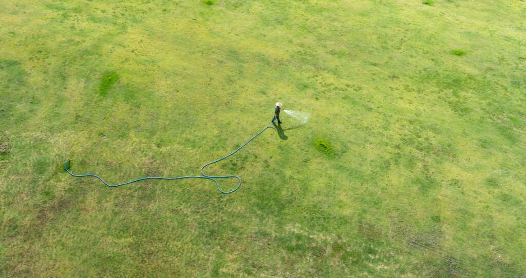 Person hosing down artificial grass in a backyard — a common turf cleaning mistake